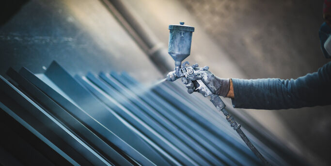 Man painting metal products with a spray gun